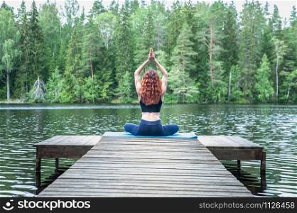 Young woman doing yoga on the pier of a beautiful lake. Concept of healthy life and natural balance
