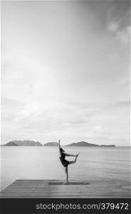 Young woman doing yoga on the wooden pier by the sea on clear sky day in summer at Koh lanta, Krabi, Thailand