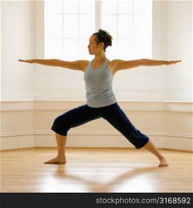 Young woman doing yoga warrior pose indoors by sunlit window.