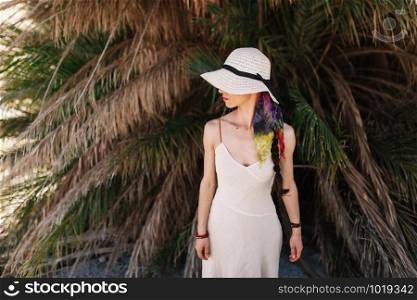 Young woman dressed in a white dress standing close to palm tree