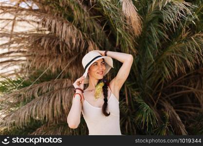 Young woman dressed in a white dress standing close to palm tree