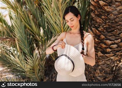 Young woman dressed in a white dress standing close to palm tree in the desert