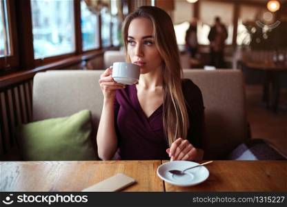 Young woman drink beverage in cafe. Beautiful girl with cup of coffee looking at the window in restaurant.