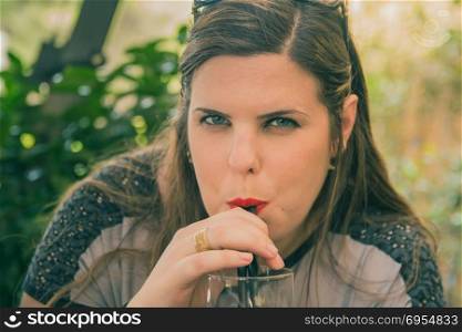 Young woman drink from a glass with drinking straw outdoor.