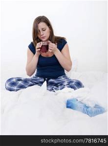 Young woman drinking a cup of tea in bed, whilst being home sick with flu