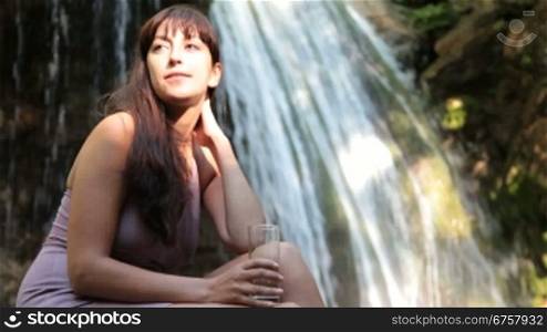 young woman drinking a glass of mineral water near the waterfall