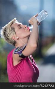 young woman drinking a water after mornig jogging workout city sunrise in background