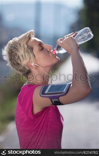 young woman drinking a water after mornig jogging workout city sunrise in background