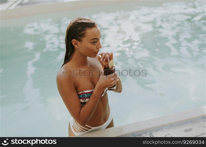 Young woman drinking coctail by swimming pool at hot summer day