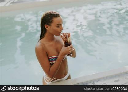 Young woman drinking coctail by swimming pool at hot summer day