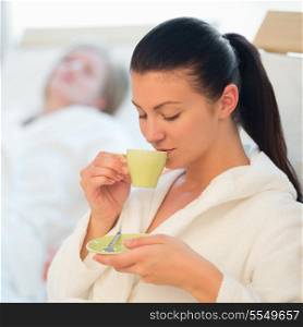 Young woman drinking coffee at spa with friend in background