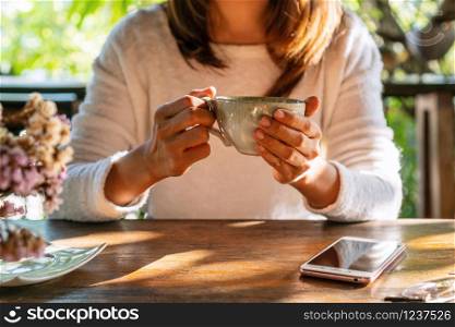 Young woman drinking coffee on wooden table with smart phone in cafe during free time.