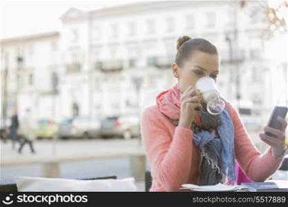 Young woman drinking coffee while using cell phone at sidewalk cafe