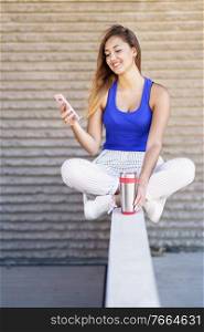 Young woman drinking from a metal water bottle wearing casual clothes. Girl sitting outdoors.. Girl drinking from a metal water bottle wearing casual clothes