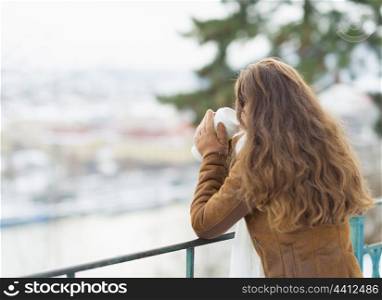 Young woman drinking hot beverage and looking into distance in winter outdoors. rear view