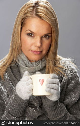 Young Woman Drinking Hot Drink Wearing Knitwear In Studio In Front Of Christmas Tree