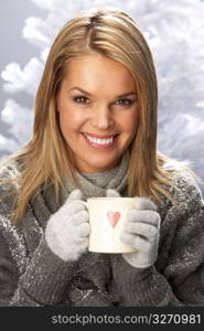 Young Woman Drinking Hot Drink Wearing Knitwear In Studio In Front Of Christmas Tree