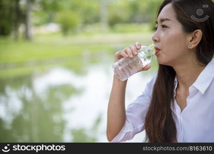 Young Woman Drinking Water from bottle in green garden Park. Asian female drinking water bottle healthy person happy and smiling. Happiness Beautiful asian chinese women holding mineral water bottle