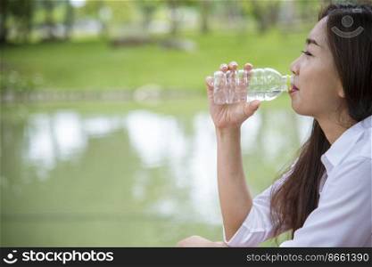 Young Woman Drinking Water from bottle in green garden Park. Asian female drinking water bottle healthy person happy and smiling. Happiness Beautiful asian chinese women holding mineral water bottle