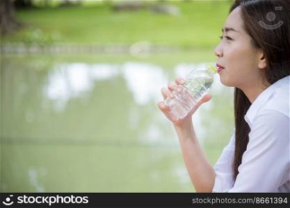 Young Woman Drinking Water from bottle in green garden Park. Asian female drinking water bottle healthy person happy and smiling. Happiness Beautiful asian chinese women holding mineral water bottle