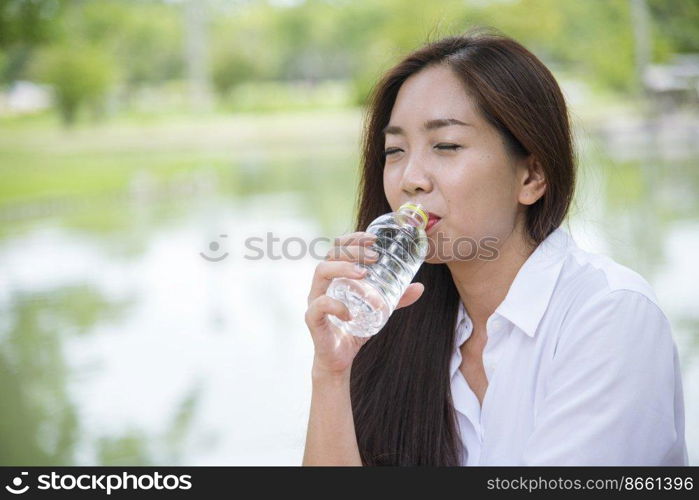 Young Woman Drinking Water from bottle in green garden Park. Asian female drinking water bottle healthy person happy and smiling. Happiness Beautiful asian chinese women holding mineral water bottle