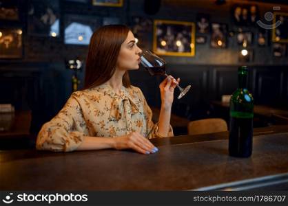Young woman drinks red wine at the counter in bar. One female person in pub, human emotions, leisure activities, nightlife. Young woman drinks red wine at the counter in bar