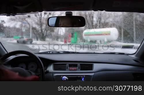 Young woman driver driving car to fuel at gas station in wintertime. View from inside of car. Beautiful girl driving her automobile on winter road heading to petrol station.