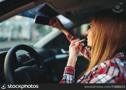 Young woman driver paints her lips with lipstick in a car. Female person preens in vehicle, driving automobile concept. Woman driver paints her lips with lipstick in car