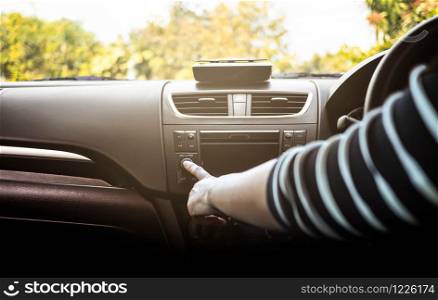 Young woman driving a car and turning button of radio in car on sunny day.