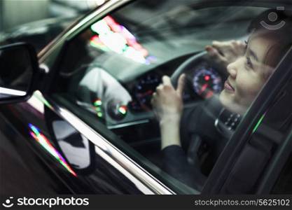 Young woman driving and looking through car window at the city night lights