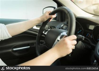 Young woman driving car and holding hands on steering wheel