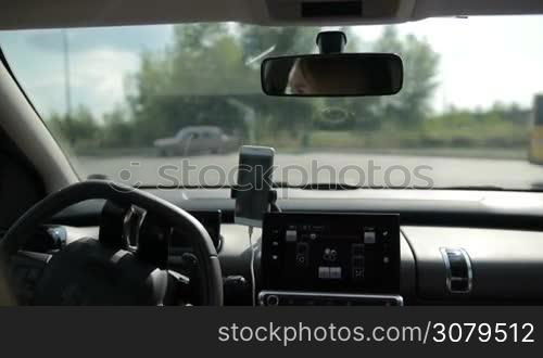 Young woman driving car and making a turn to refuel vehicle on petrol station during summer road trip. View from inside of auto. Female driver driving car to full service gas station.