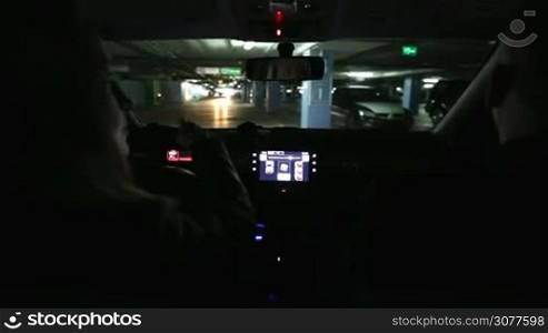 Young woman driving car in parking garage with few parked cars, looking for vacant space in parking lot. View from car interior. Underground covered parking lot with few cars and empty spaces for more vehicles