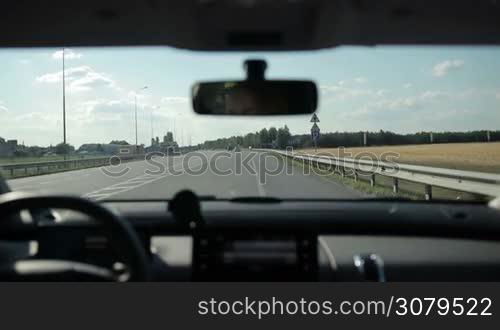 Young woman driving car on highway, passing by crossroad with road signs on background. Female travelling by car during summer vacation trip. View from inside of vehicle.