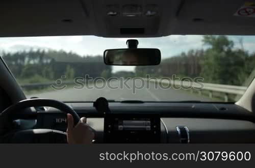 Young woman driving car on straight highway on sunny summer day. View form vehicle&acute;s interior. Female driver controlling auto on high speed on freeway.