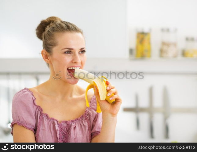 Young woman eating banana in kitchen