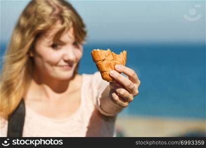 Young woman eating croissant meal food outdoor. Pretty girl having breakfast by sea ocean. Summer pleasure.. Young woman eating croissant food outdoor.