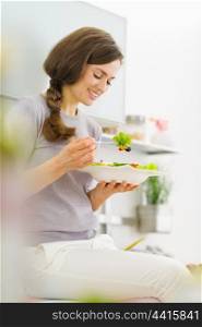 Young woman eating fresh salad in modern kitchen