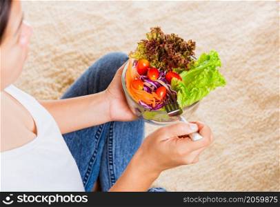 Young woman eating fresh salad meal vegetarian spinach in a bowl, top view of female hands holding bowl with green lettuce salad on legs, Clean detox healthy food concept