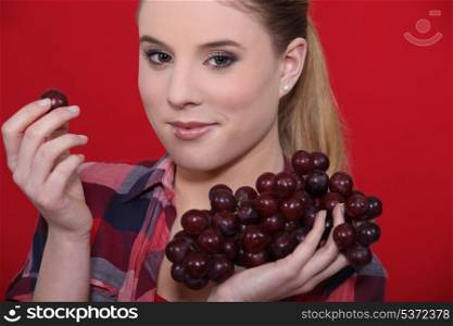 Young woman eating grapes on red background