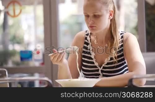 Young woman eating hot spaghetti, sometimes blowing on it.