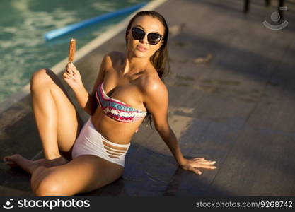 Young woman eating icecream near the swimming pool at hot summer day