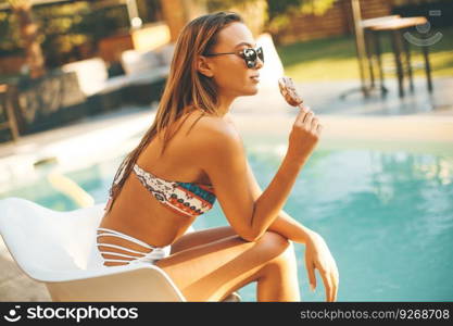 Young woman eating icecream near the swimming pool at hott summer day