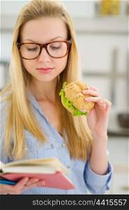Young woman eating sandwich and reading book