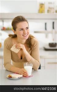 Young woman eating snacks in modern kitchen and looking on copy space