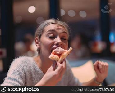 Young woman eats a pizza from delivery service while at work at the modern office in late night . Young woman eats a pizza from delivery service at office