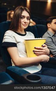 Young woman eats popcorn while watching movie in cinema. Showtime. Woman eats popcorn while watching movie in cinema