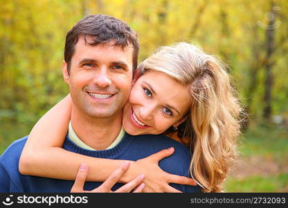 Young woman embraces man from back in autumn wood