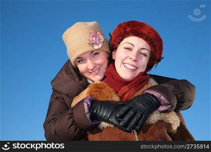 young woman embraces other against blue sky in winter