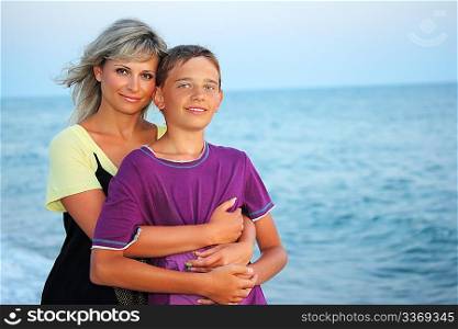 young woman embraces smiling boy on beach in evening